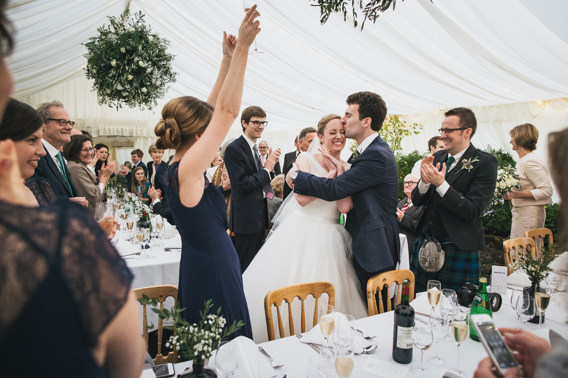 Bride and groom in marquee with wedding guests cheering and clapping