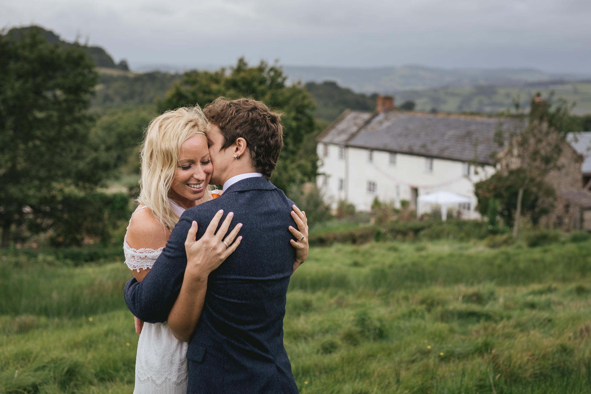 Bride and groom cuddling with River Cottage farmhouse in the background