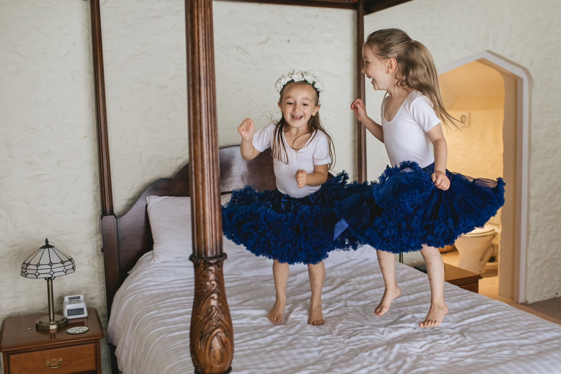 Flower girls in blue tutus jumping on a four poster bed