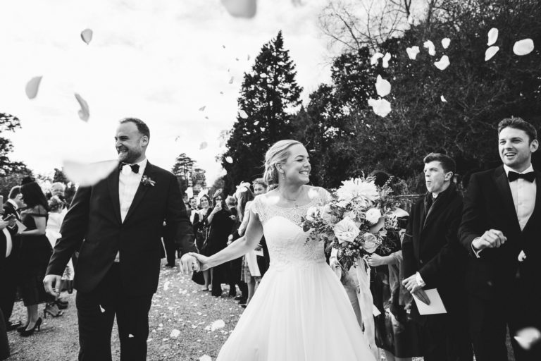Smiling bride and groom walking through confetti at Brympton House