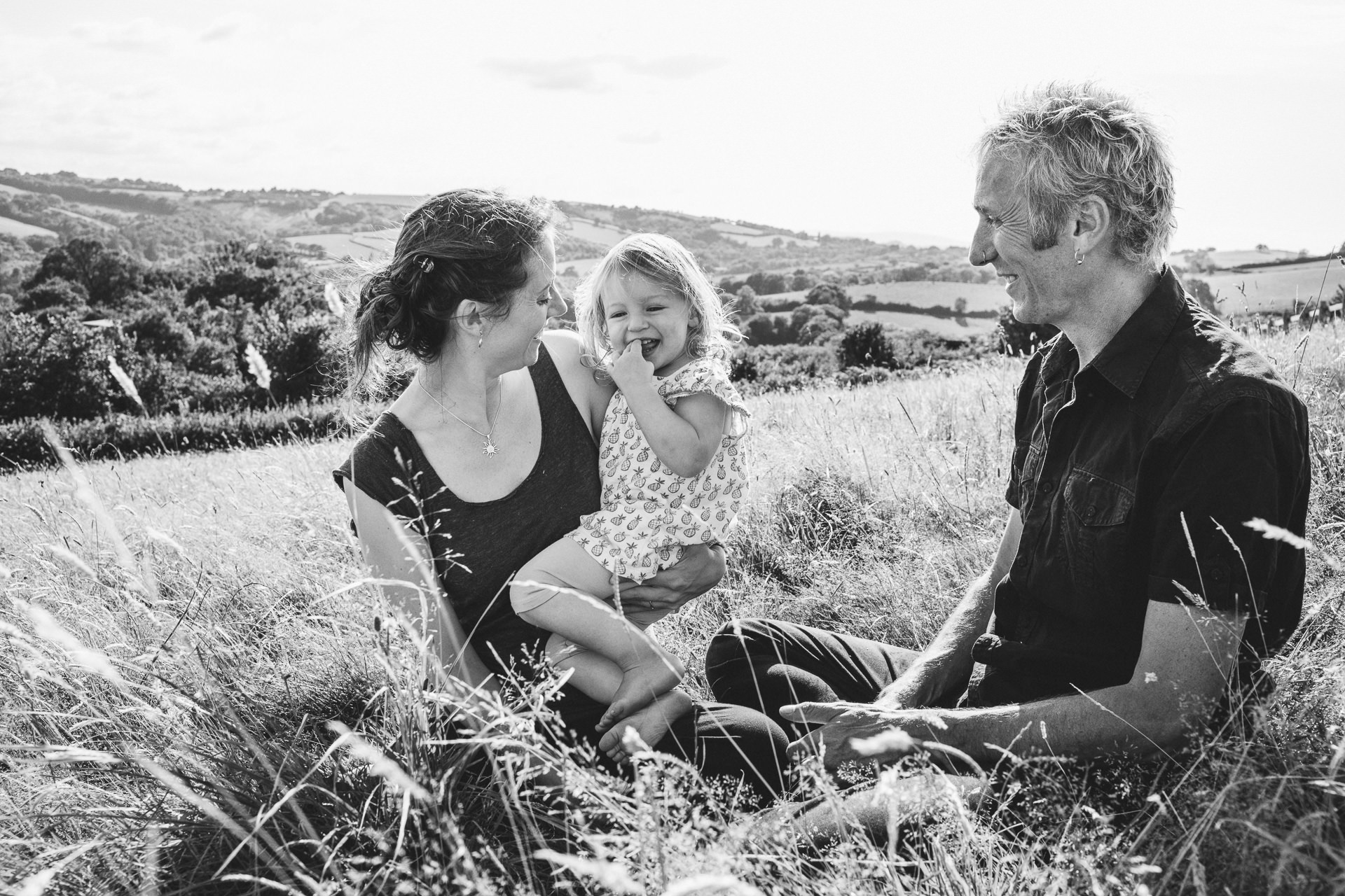Two parents with a young daughter cuddling together in a field