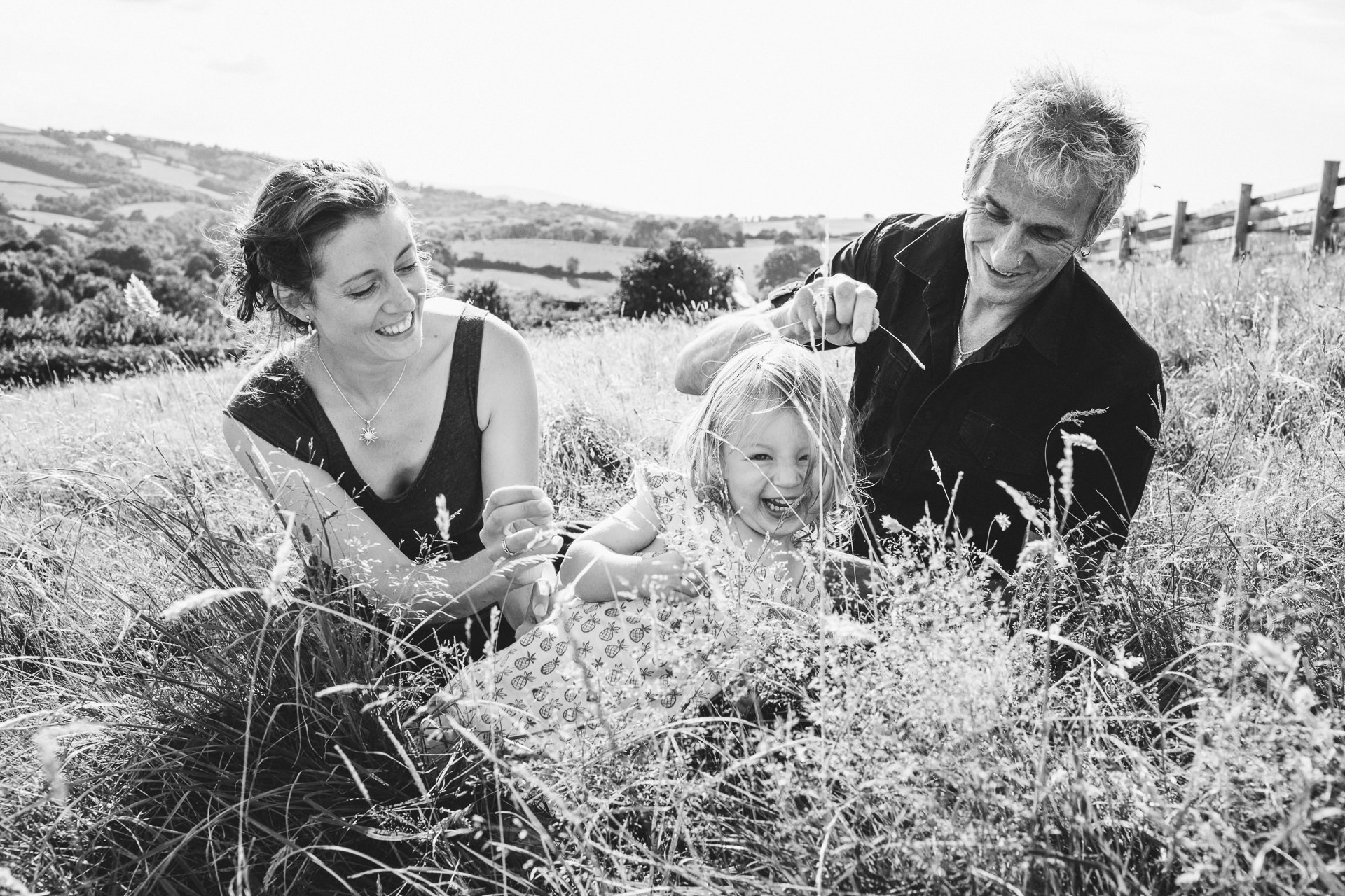 Two parents with a young daughter cuddling together in a field