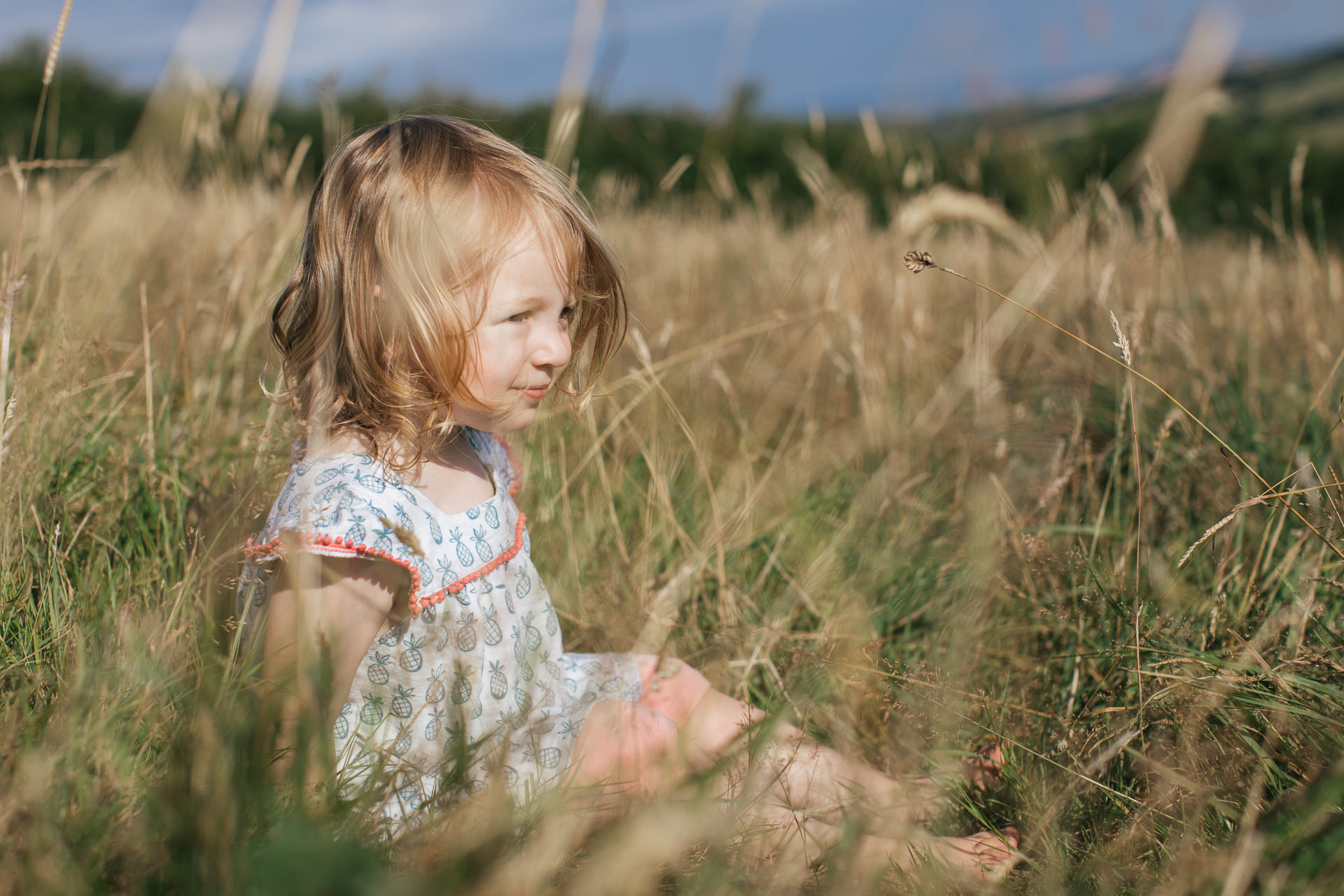 A small girl sitting in some long grass