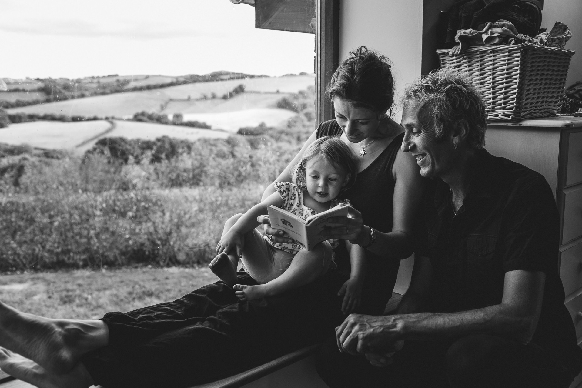 Mother, father and young daughter, reading a story together on a window seat
