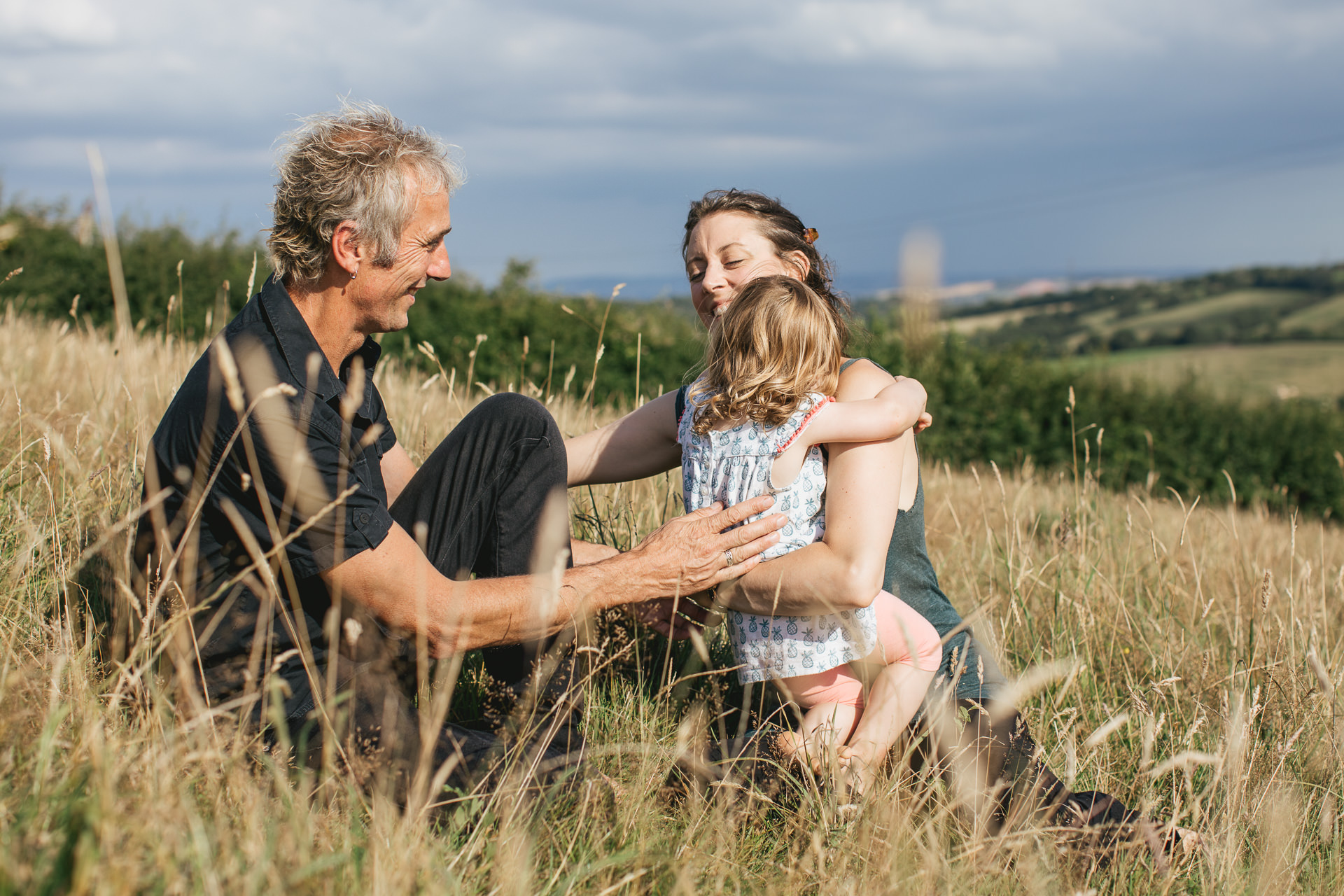 Two parents with a young daughter playing in long grass
