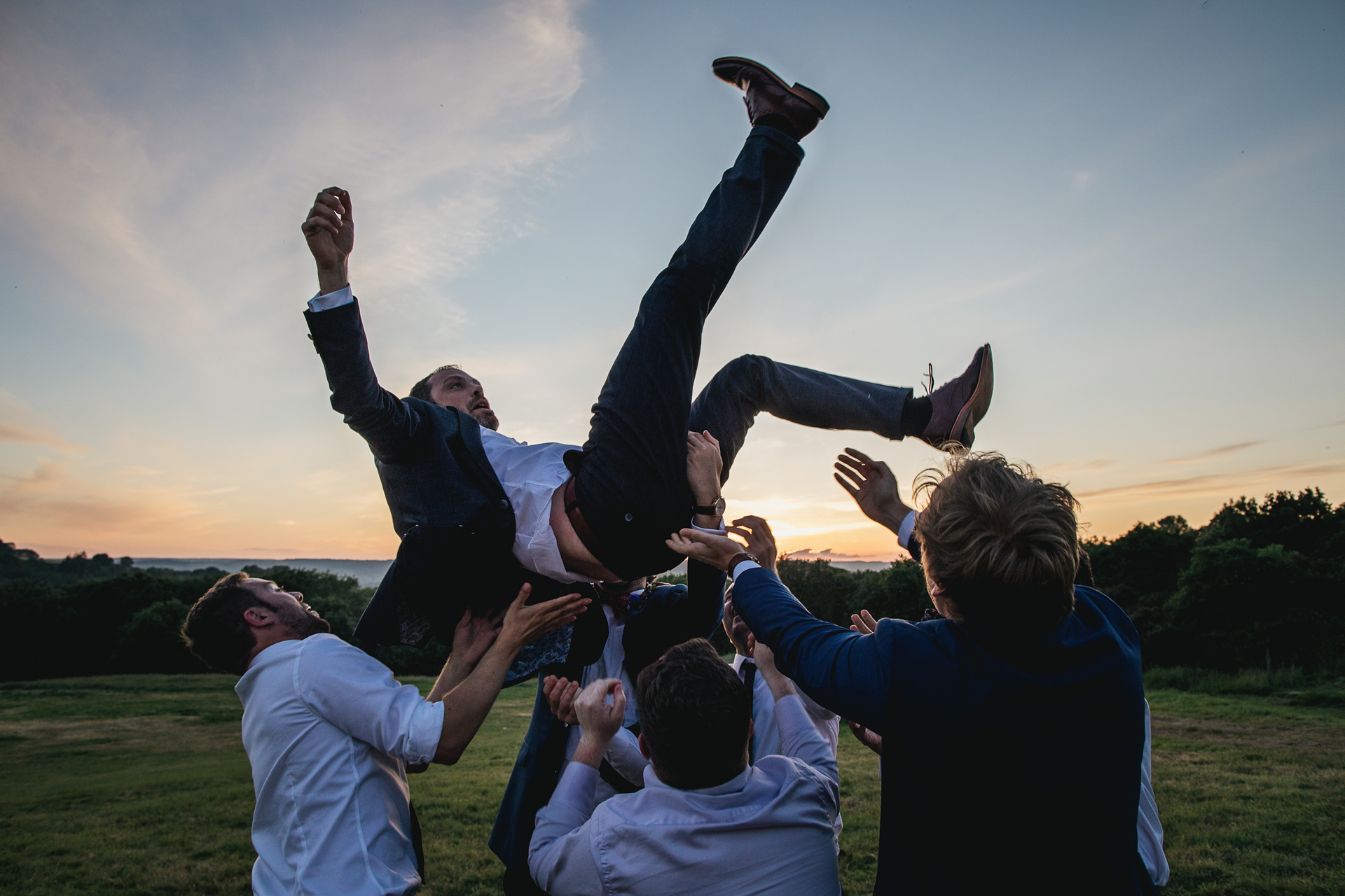 Wedding guests throwing groom up in the air 