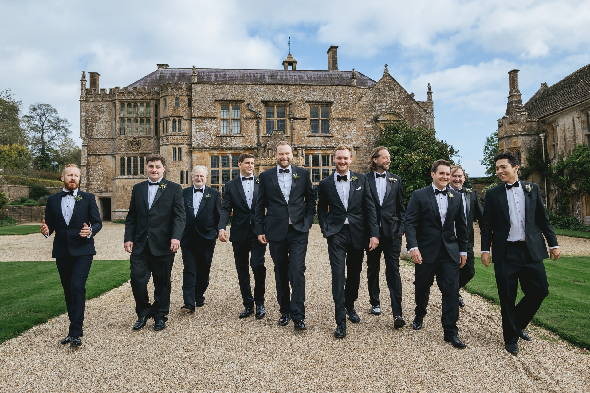 Groom and groomsmen in black tie walking down the drive in front of big country house