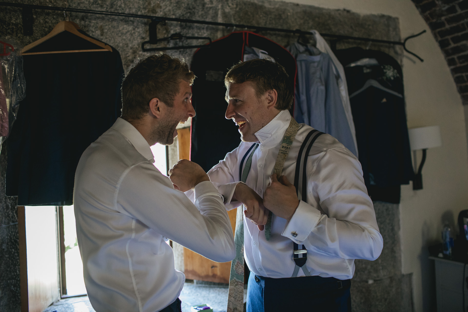 Groom getting dressed into shirt and braces