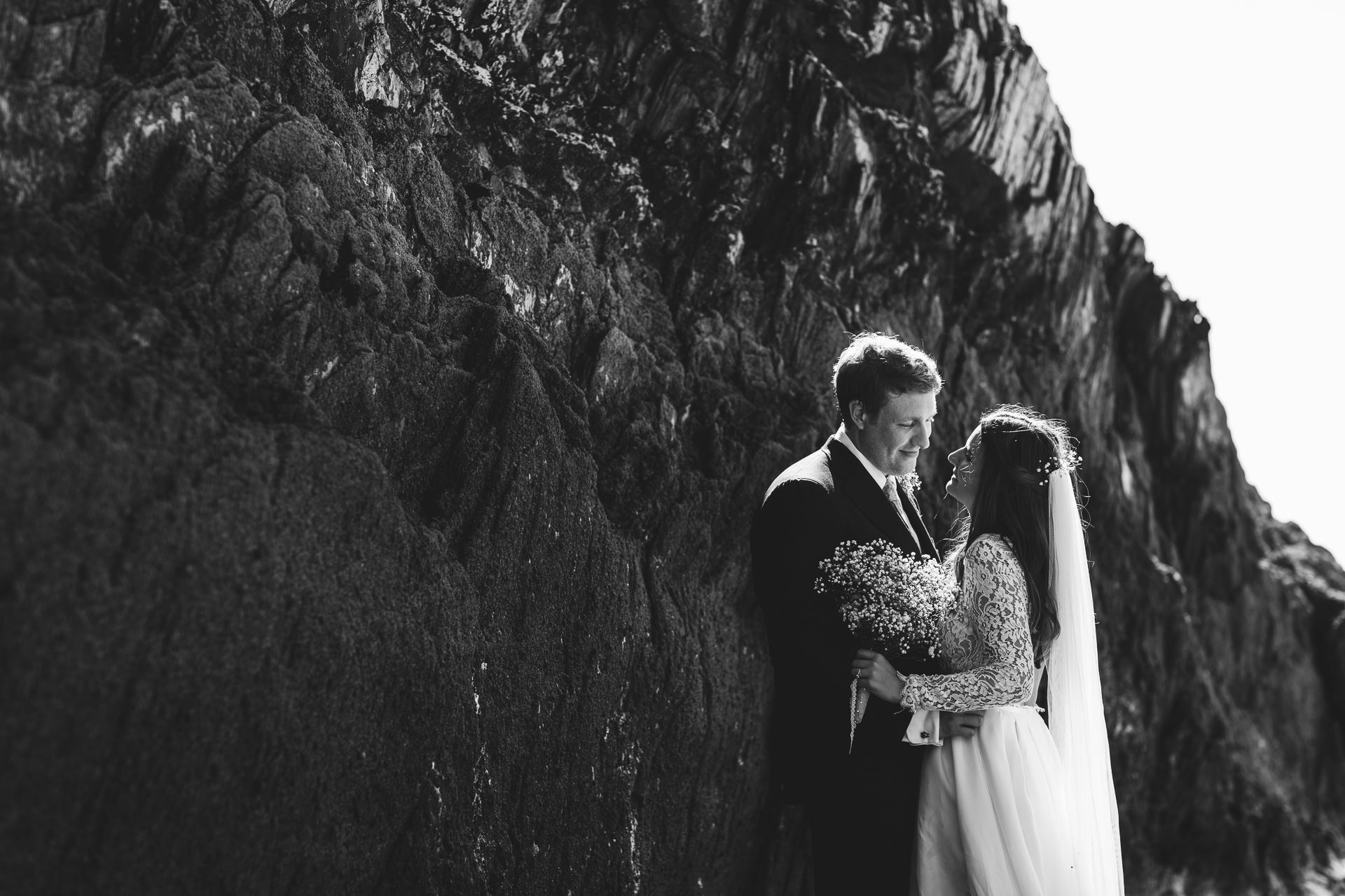 Bride and groom standing by rocks on the beach
