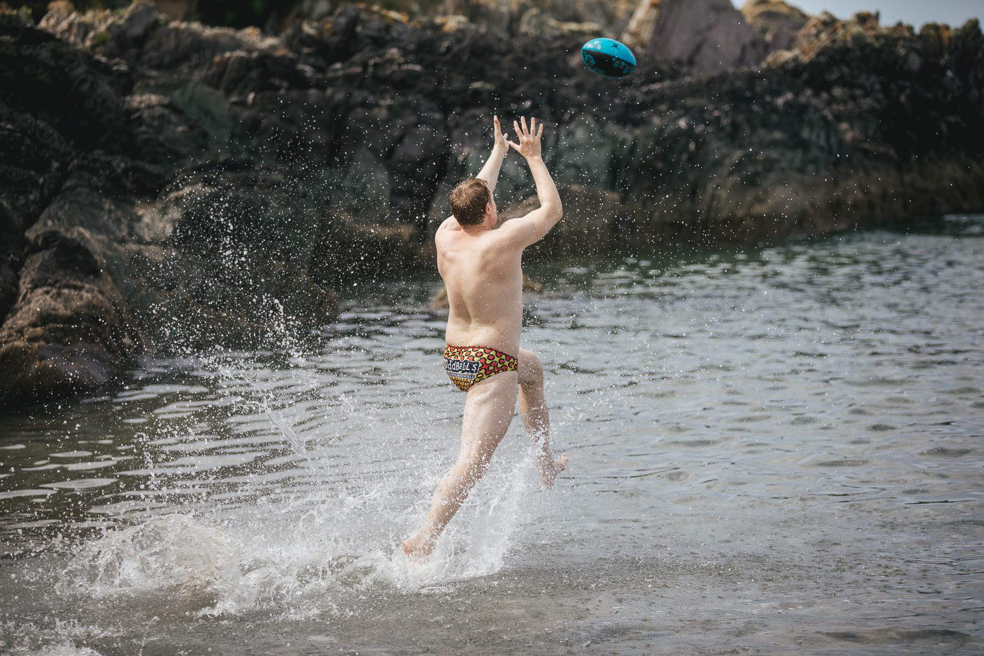 A man in trunks catching a rugby ball in the sea
