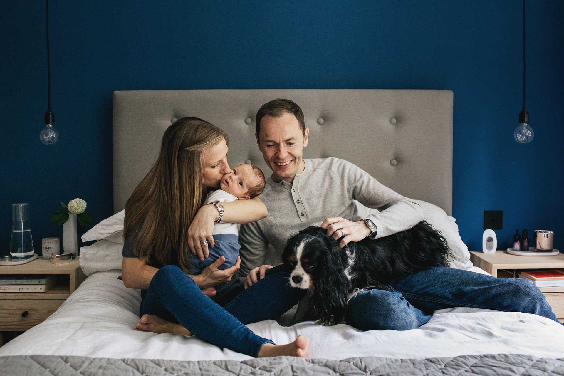 A family with newborn baby together in their bedroom at home with a dog 
