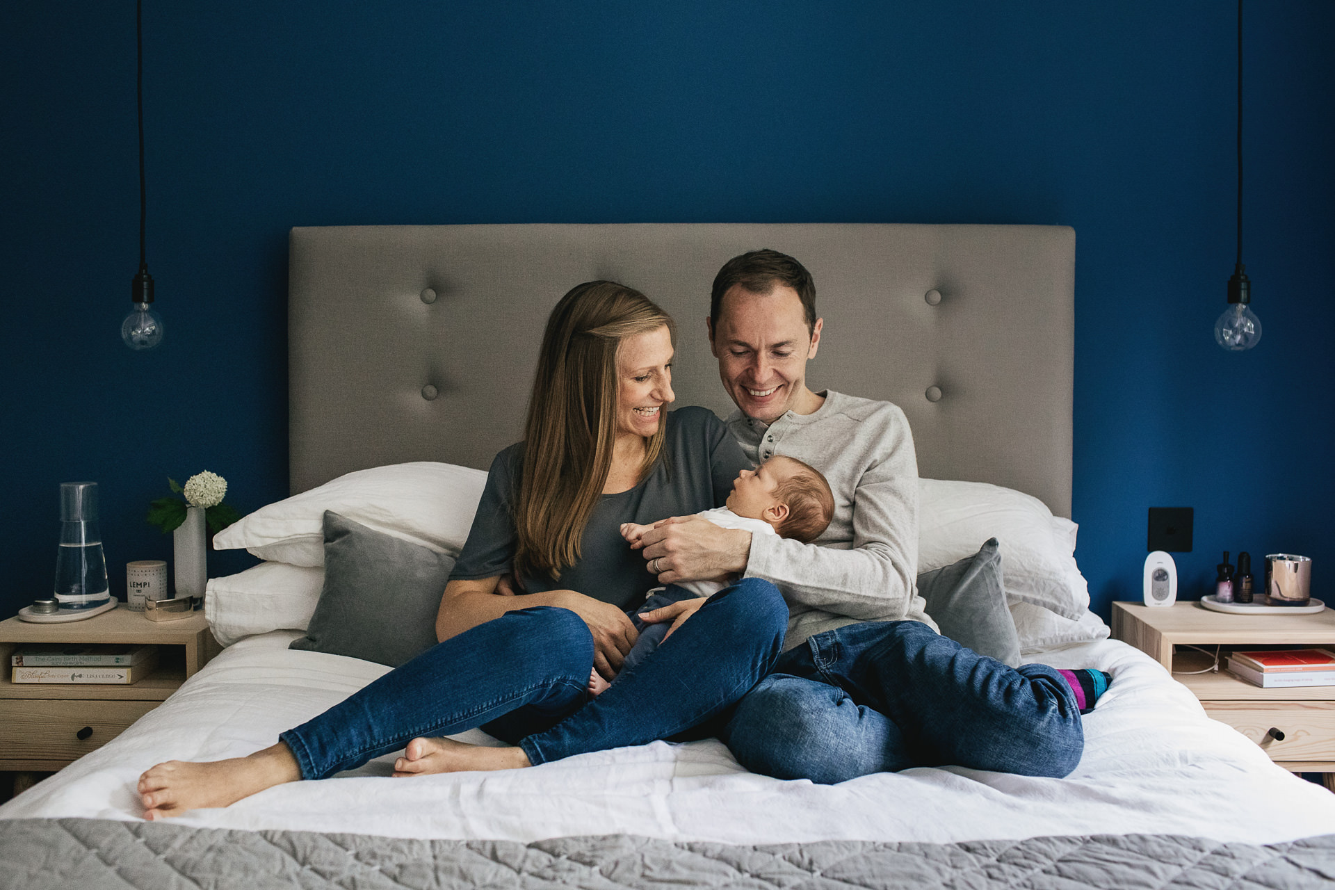 Portrait of a family with a newborn baby at home in their bedroom, smiling at each other on a bed