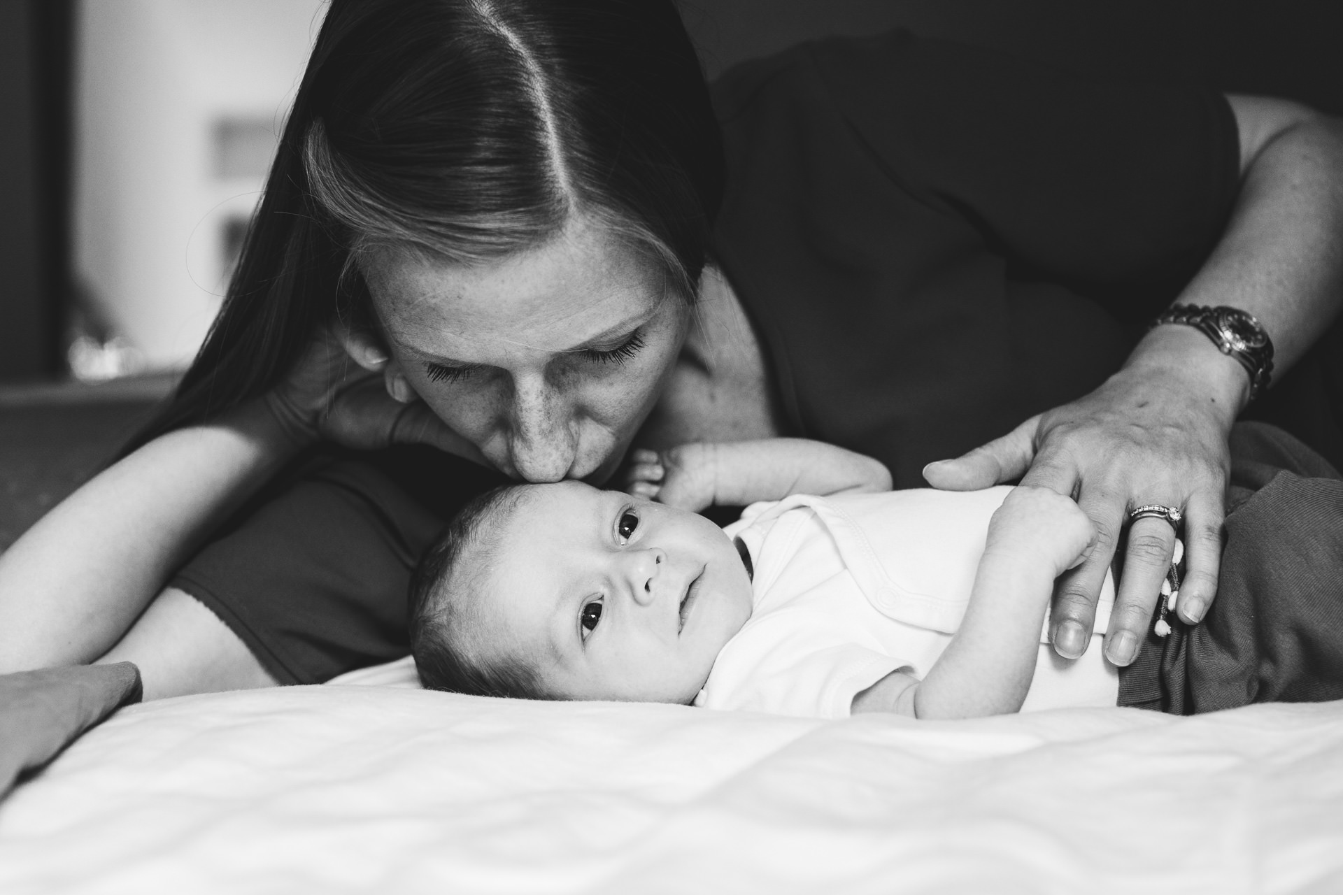 Mother kissing a baby while lying on a bed together at home