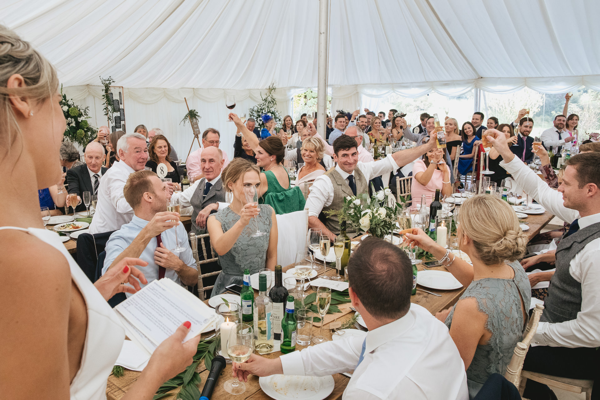 Guests raising toasts at wedding speeches inside a marquee