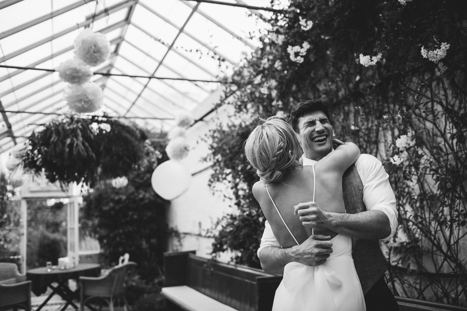 Bride and groom laughing together in glasshouse