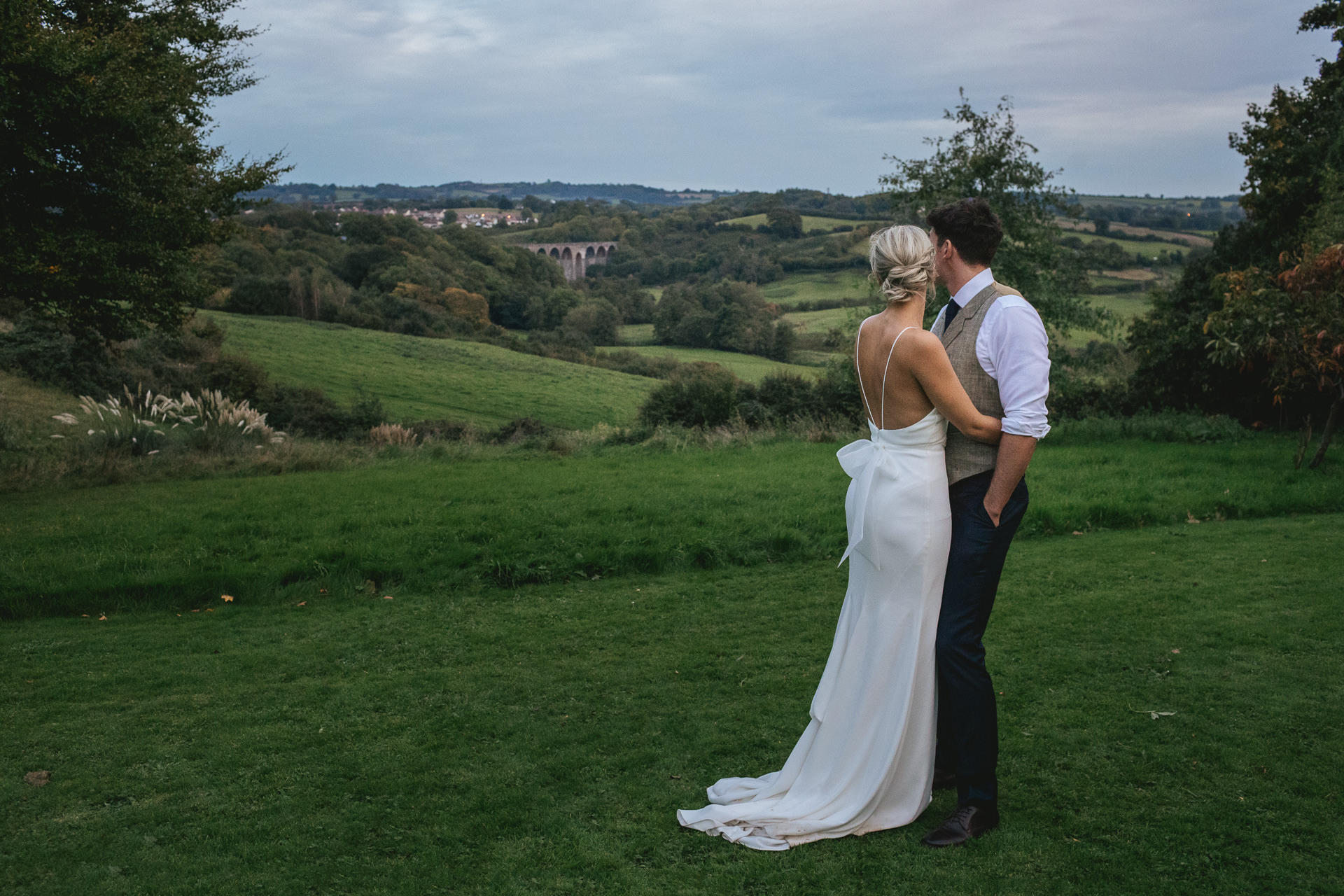 Bride and groom cuddling and looking across Somerset hills