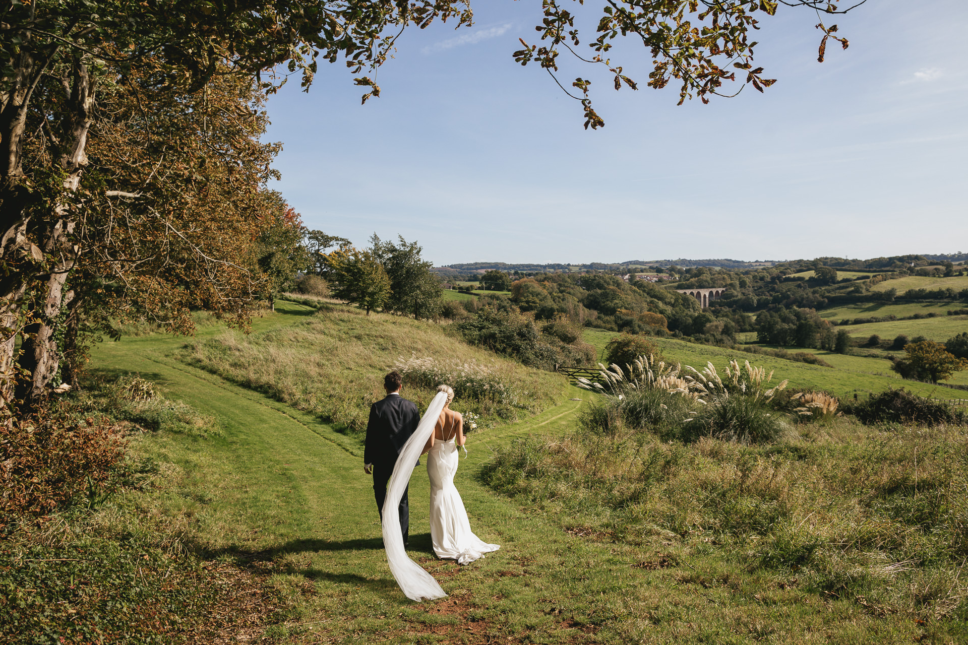 Bride and groom walking along path with veil flying in the wind