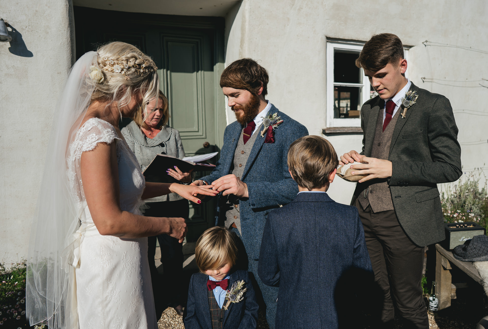 Groom putting ring on bride's finger, with sons all around them
