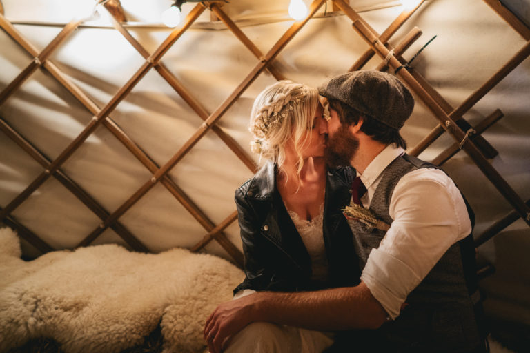 Bride in leather jacket kissing with groom in a yurt