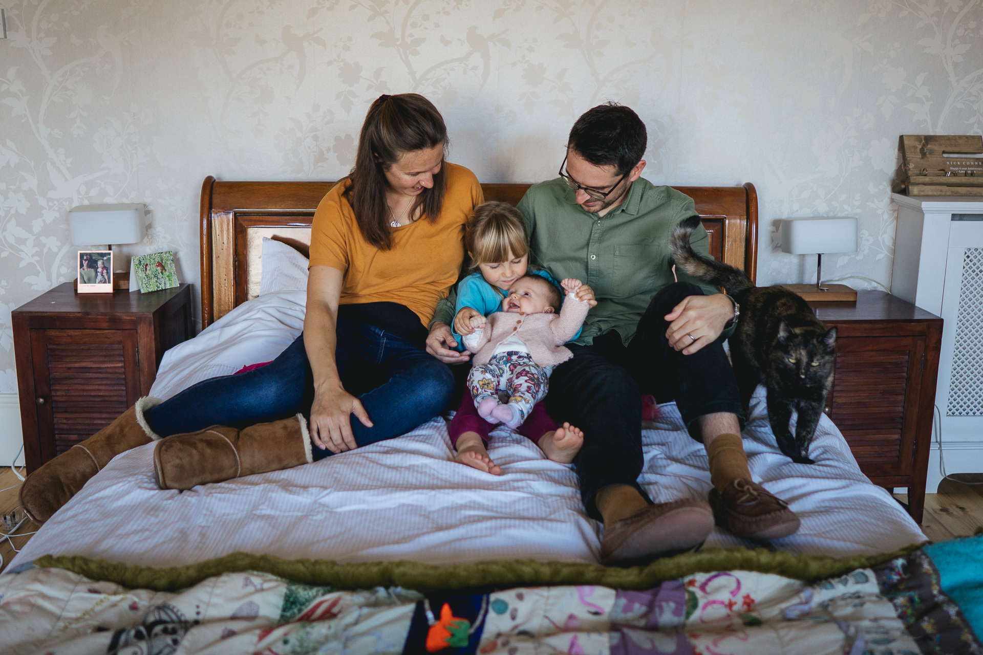 A family sitting on the bed together with a cat for a family photography session at home in Exeter