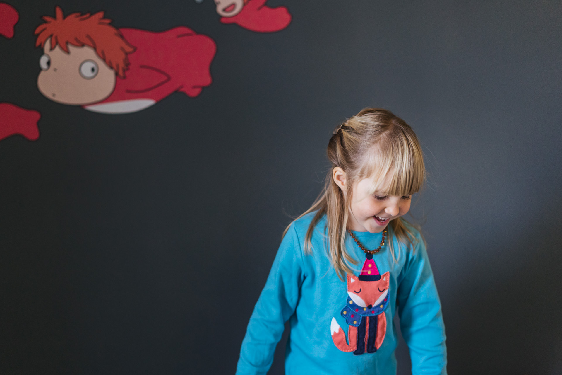 A young girl laughing with cartoon stickers on the wall behind