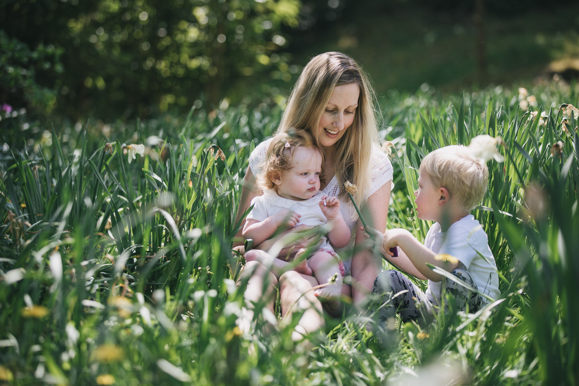 A mother sitting with two children amongst greenery