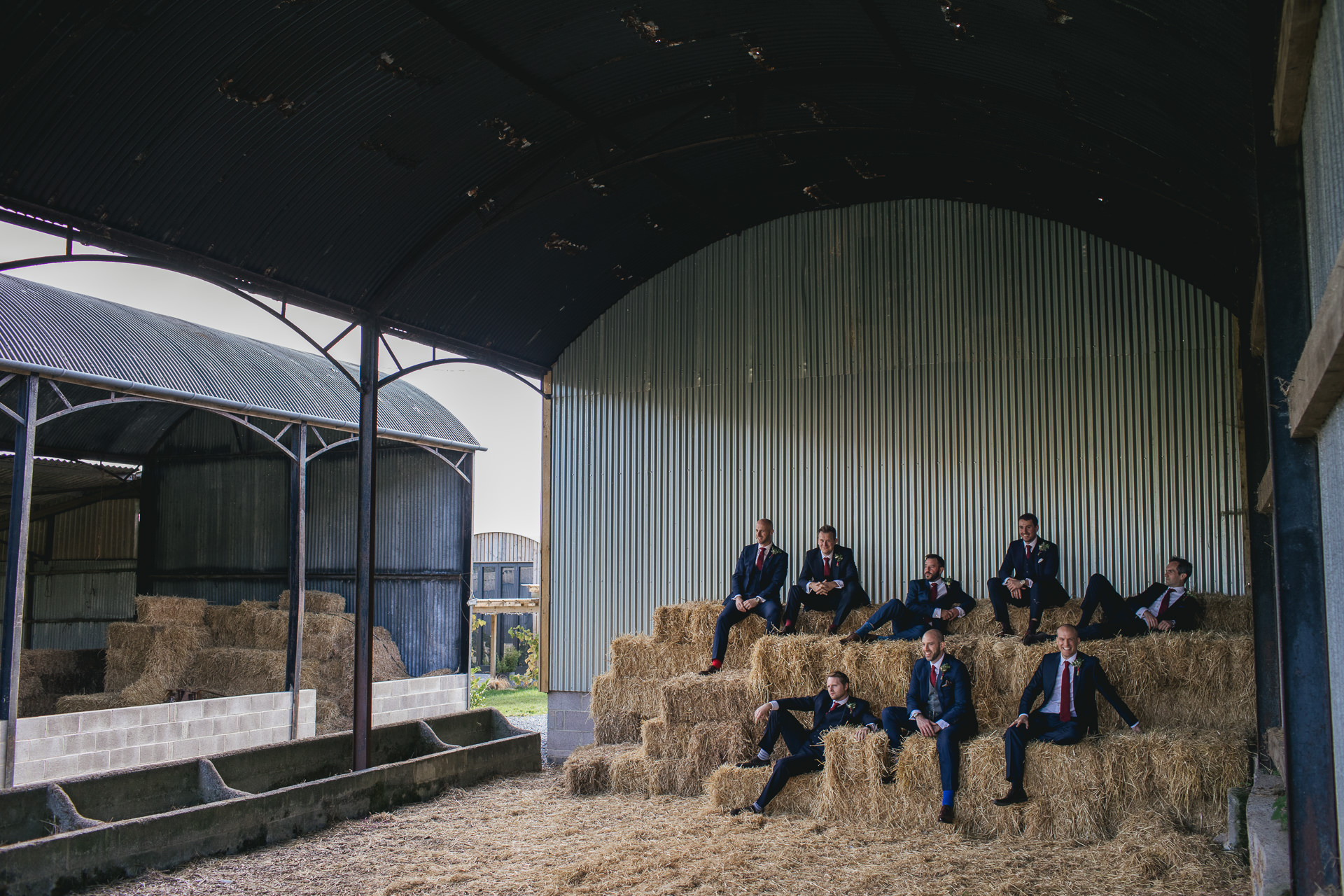 Group of groomsmen posing on hay bales in a barn