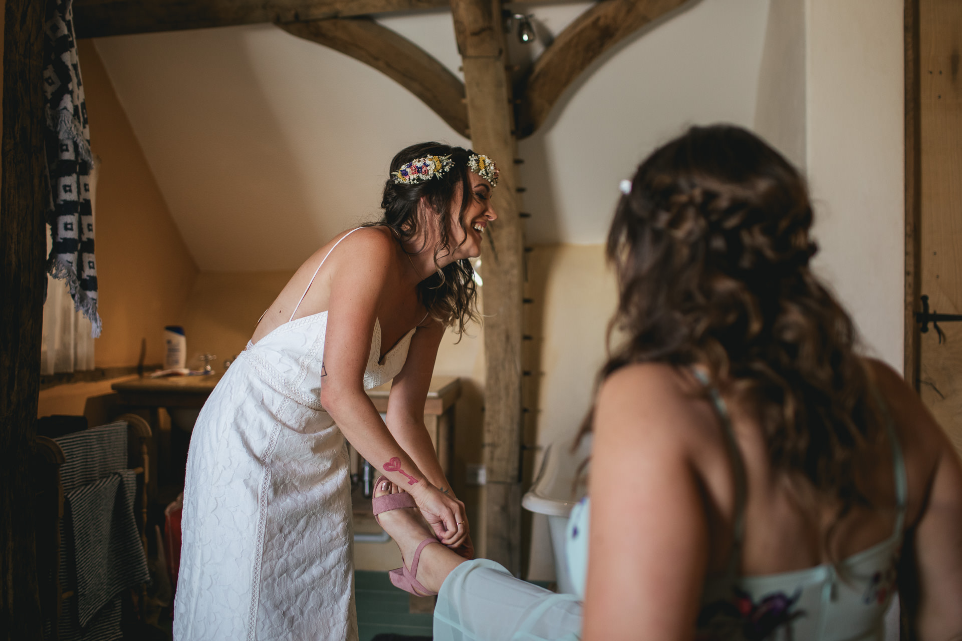 Bride putting on bridesmaid's shoes and laughing