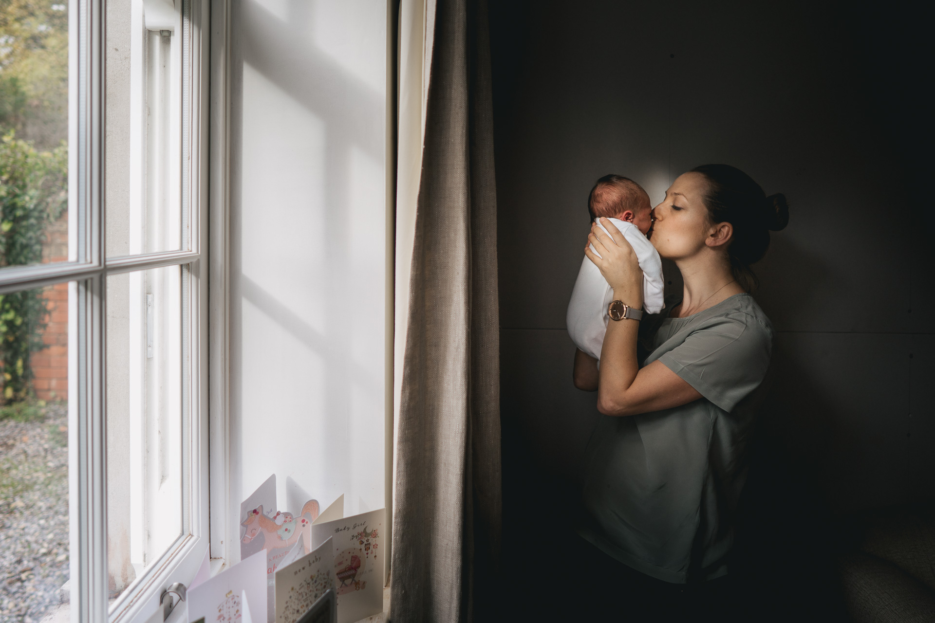 A woman kissing a newborn baby by a window