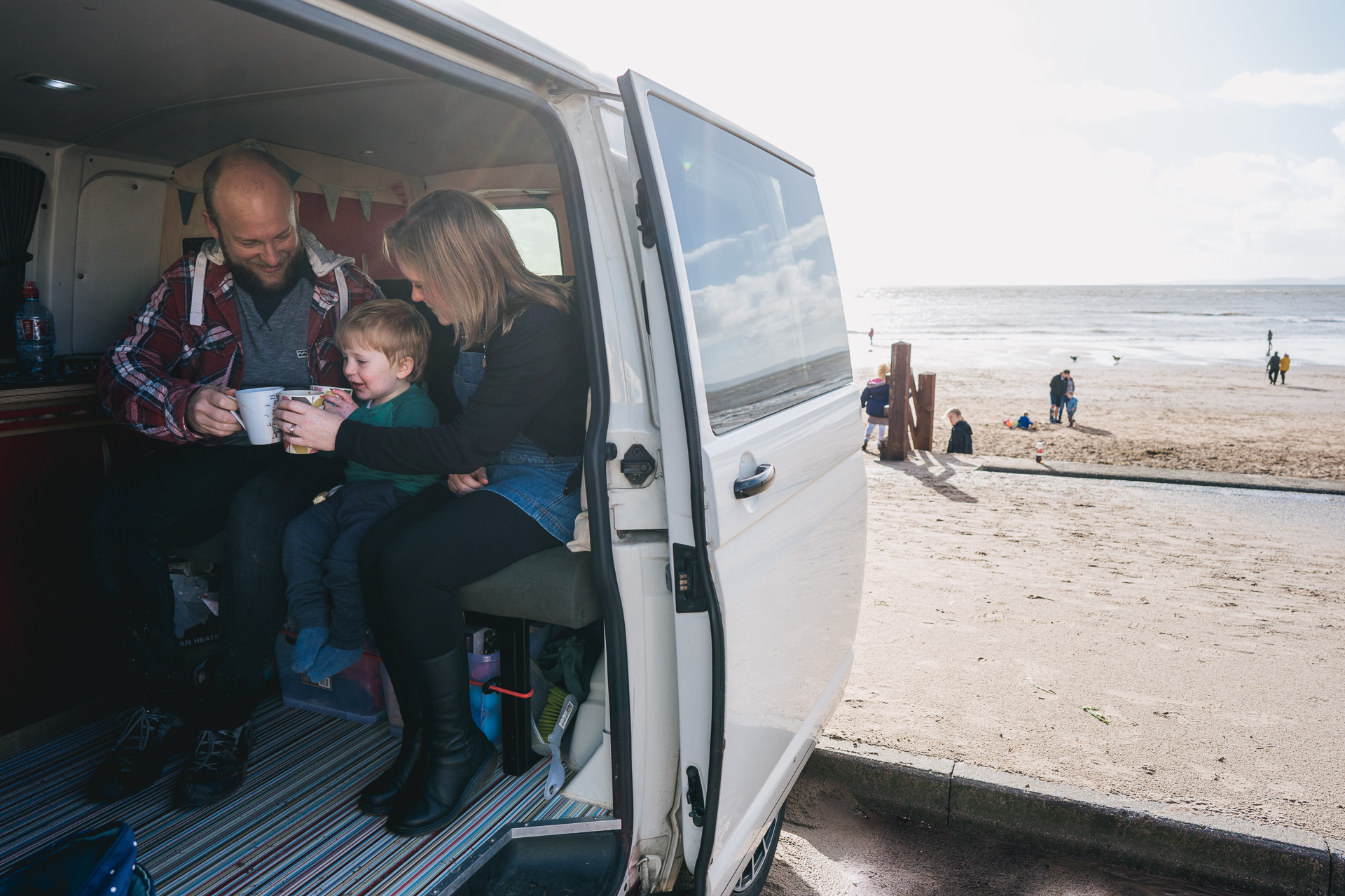 Parents with a young boy sitting in a camper van by the beach