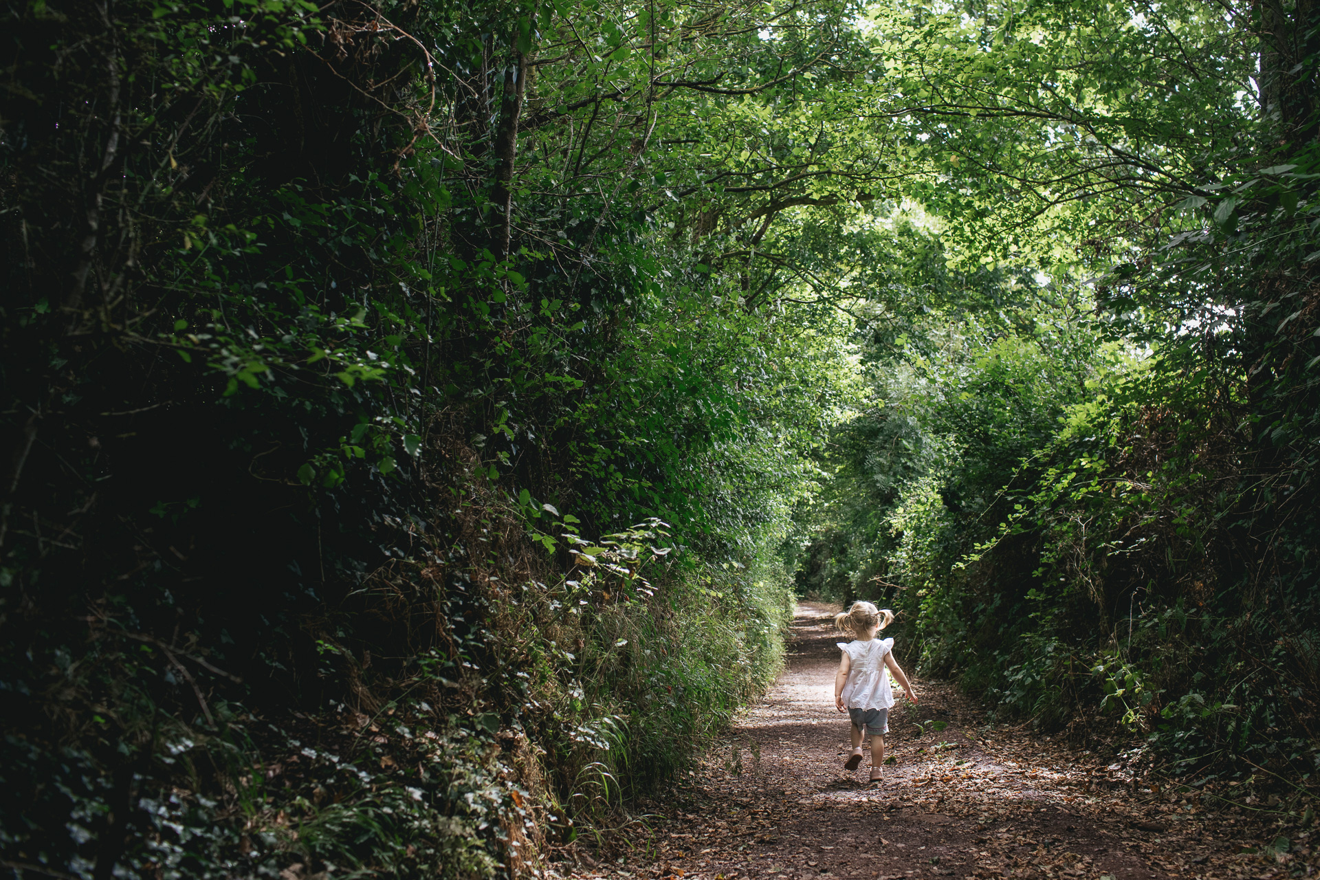 A small girl walking through a lane with trees above