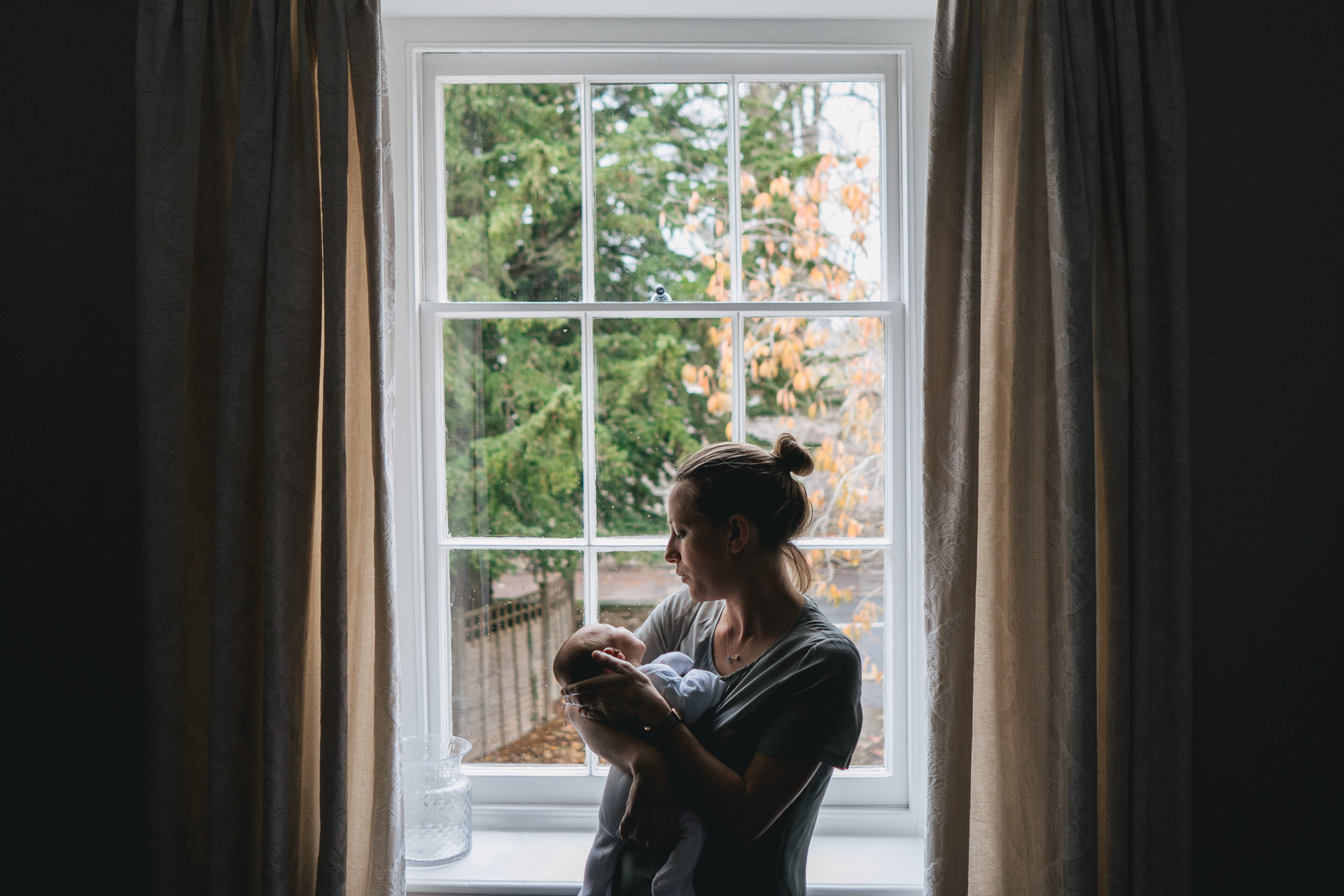 A mother with a newborn baby in front of a window
