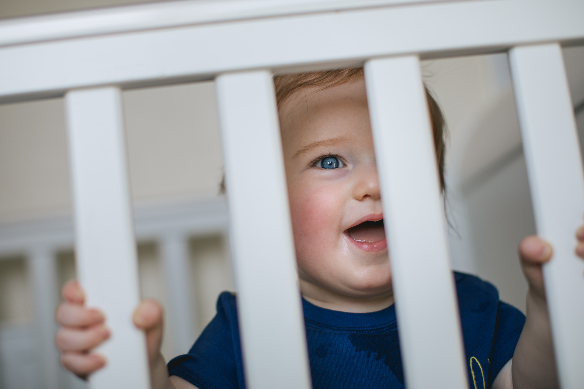 A toddler peeping through the bars of a cot