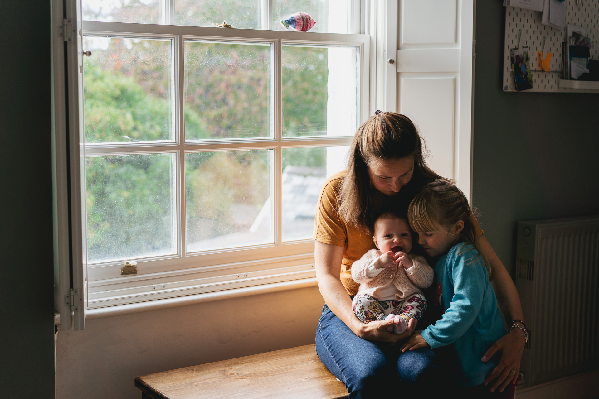 A mother cuddling two daughters by a window