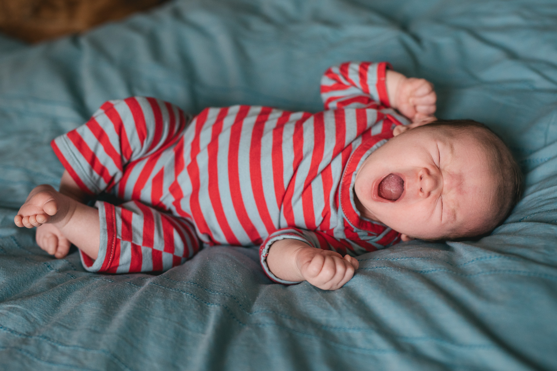 A baby in a stripey outfit, yawning