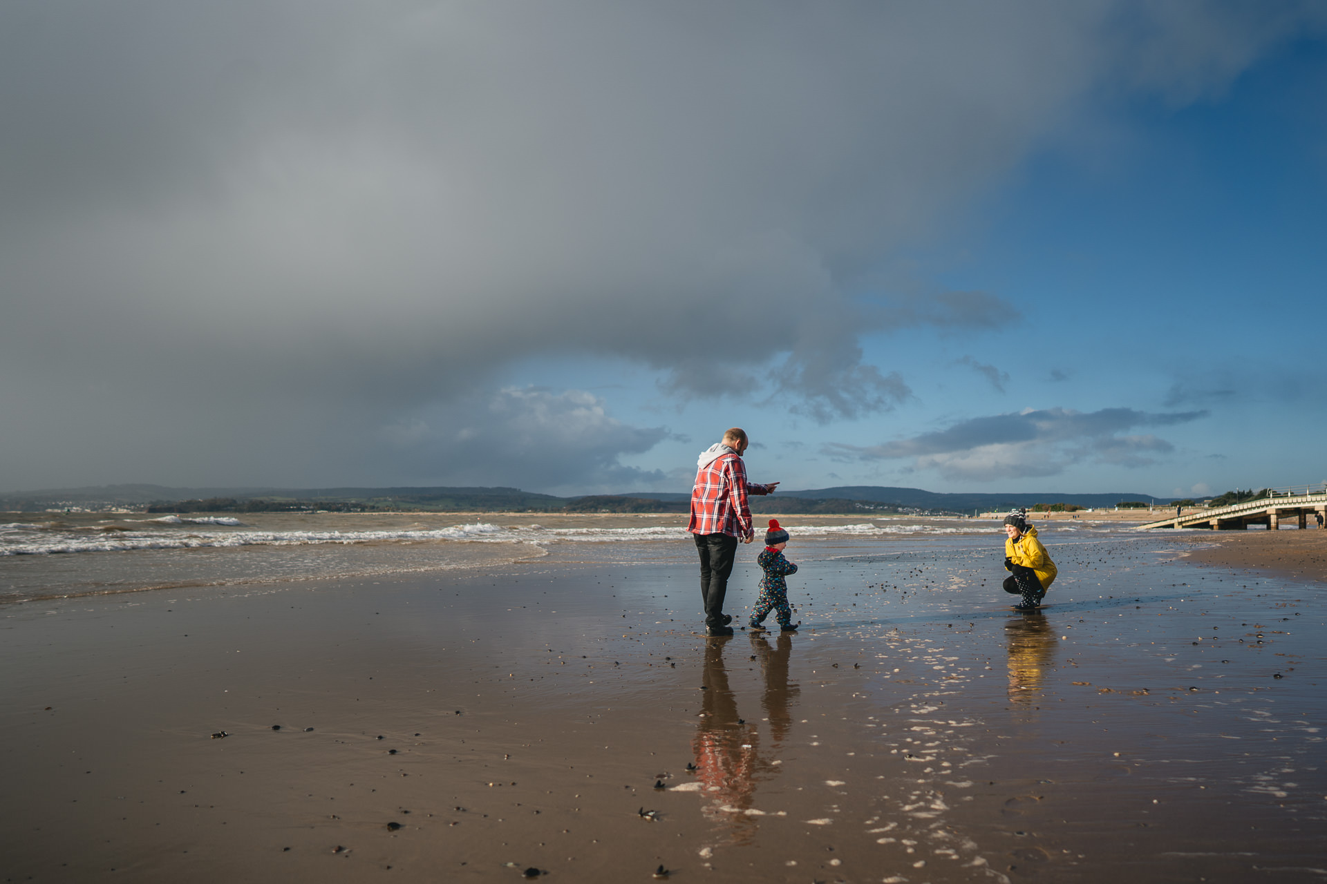 A young child walking between two parents on a beach