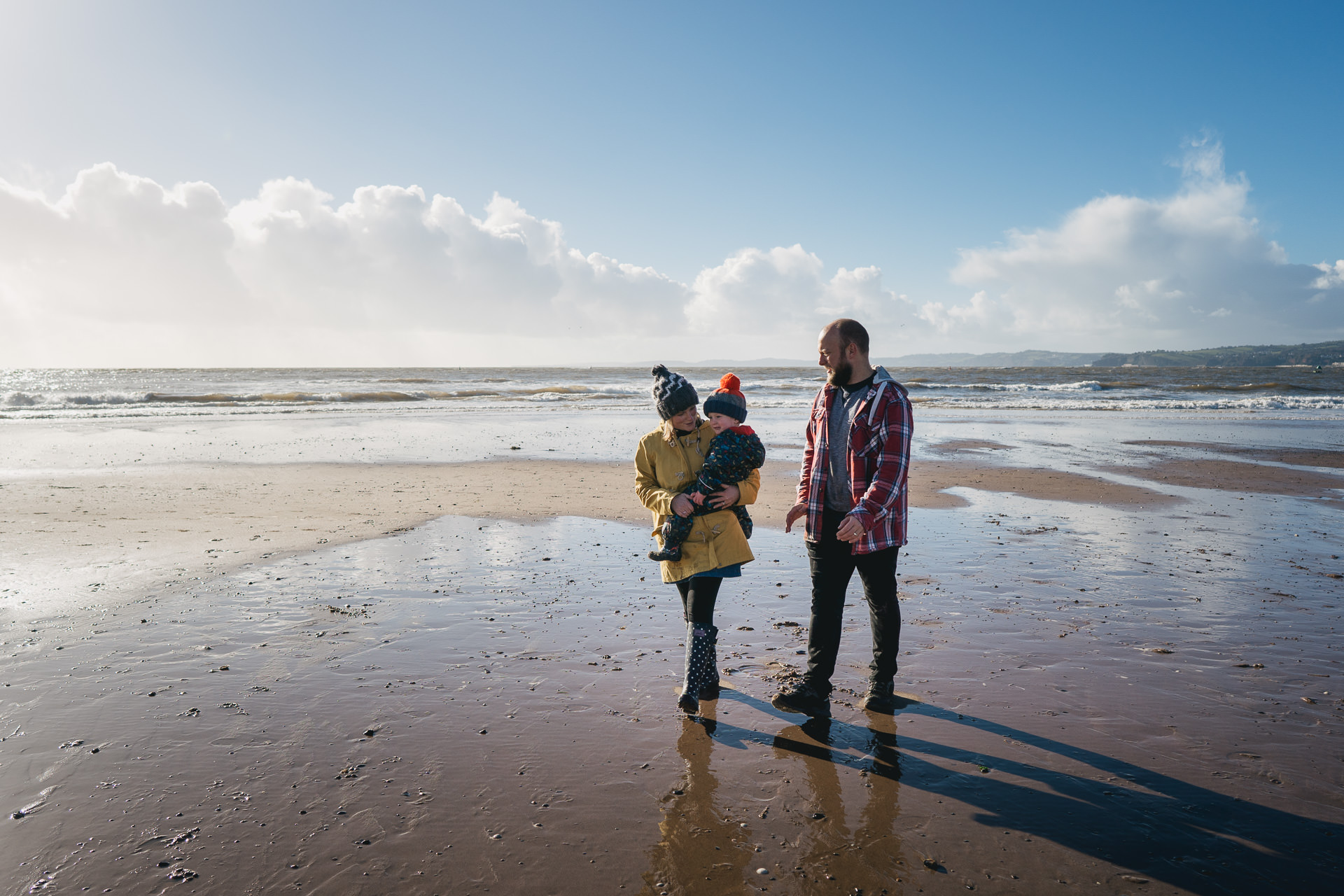 Exmouth family photography, father and mother walking on a beach carrying their son
