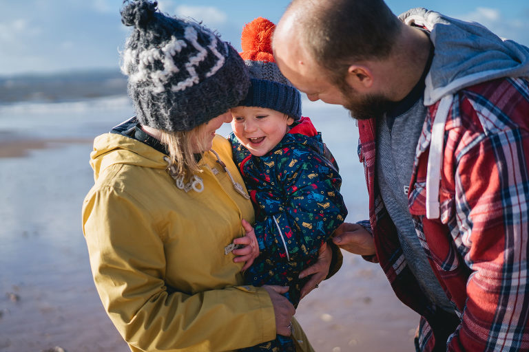 A mother and father cuddling a toddler on a beach