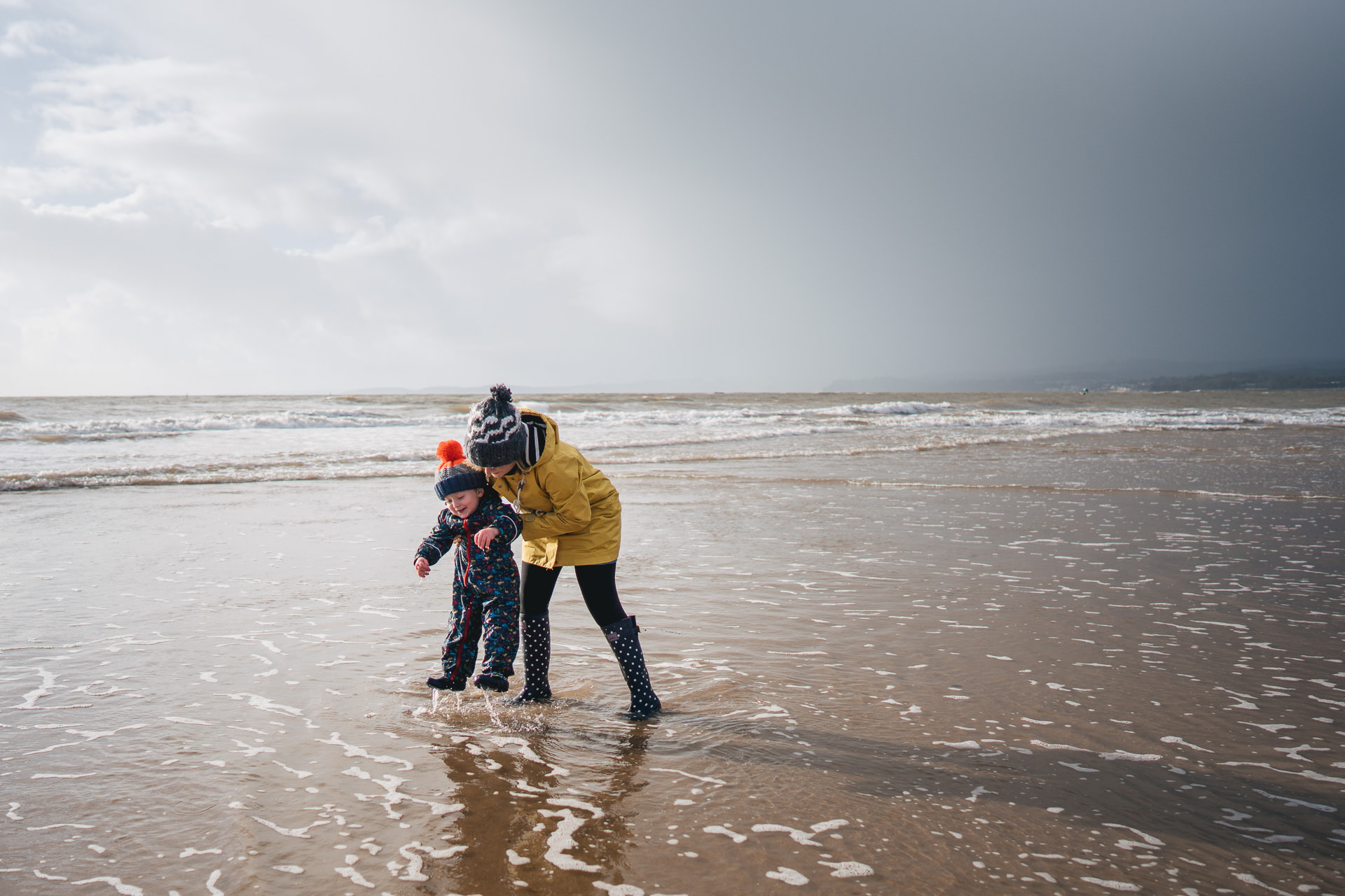 Exmouth family photography, a mother and son playing in the sea with stormy skies behind