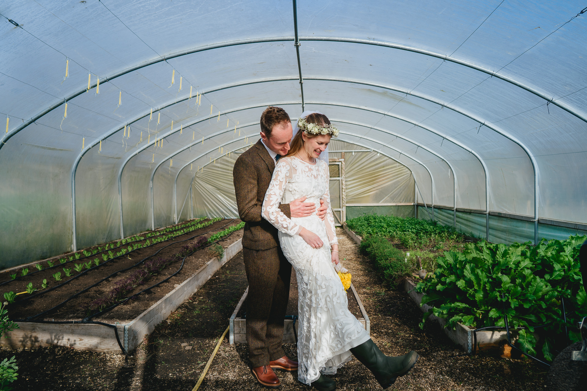 A bride wearing wellies with groom smiling in a poly tunnel
