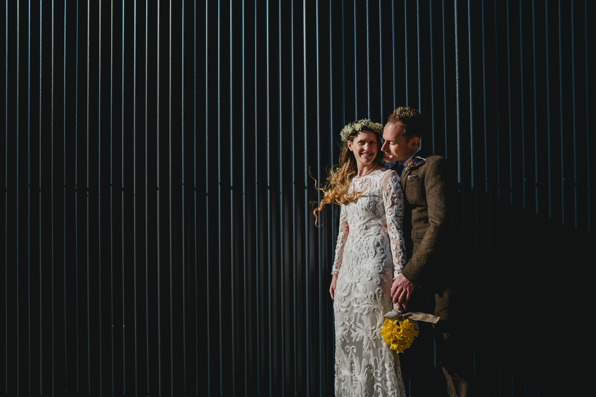 A bride and groom standing in front of a corrugated shed