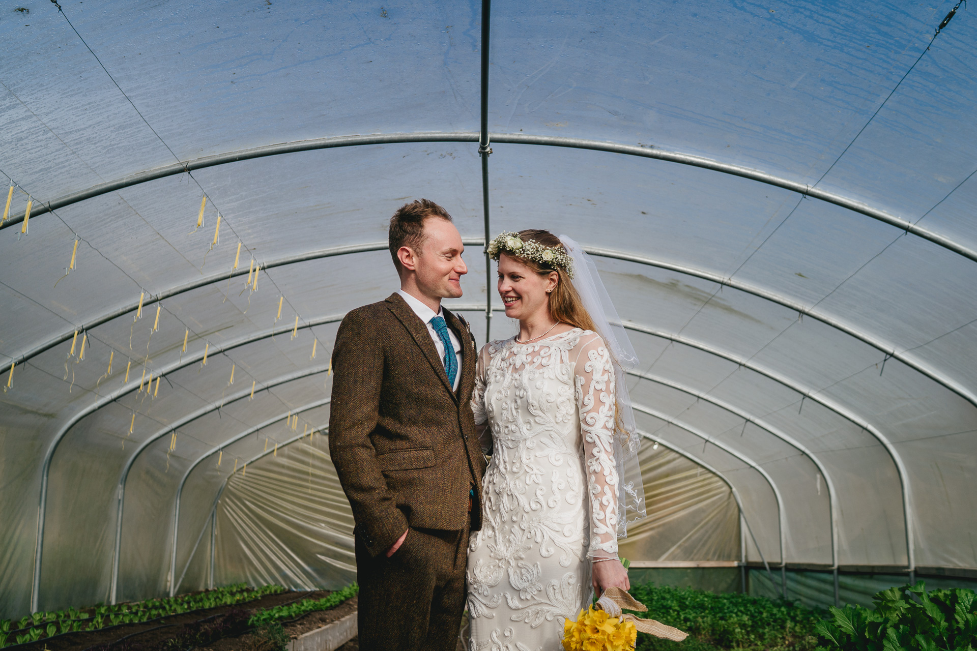 A bride and groom cuddling and smiling in a poly tunnel