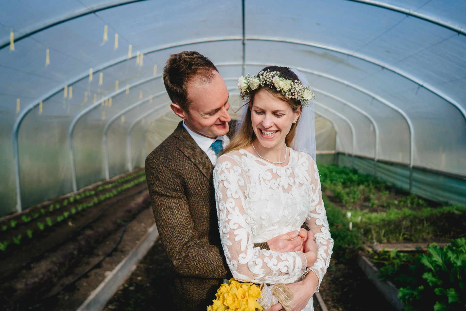 A bride and groom cuddling and smiling in a poly tunnel