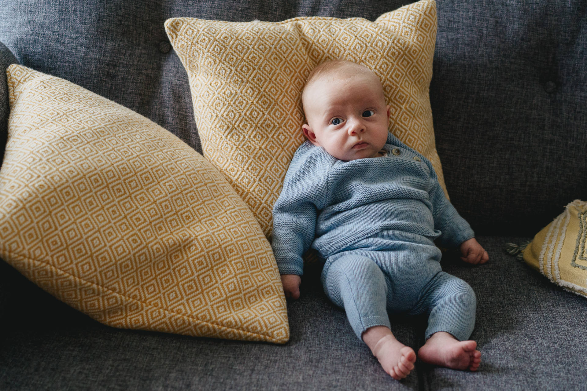 A baby on a sofa with yellow cushions 