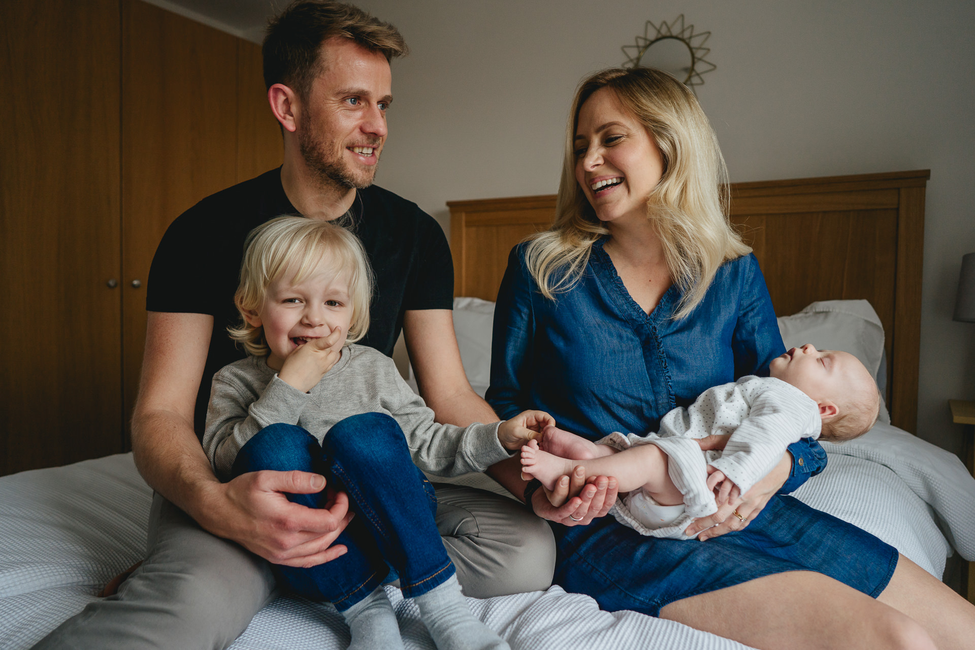 Dorset family photoshoot - a Mum, Dad, young boy and baby laughing on a bed together