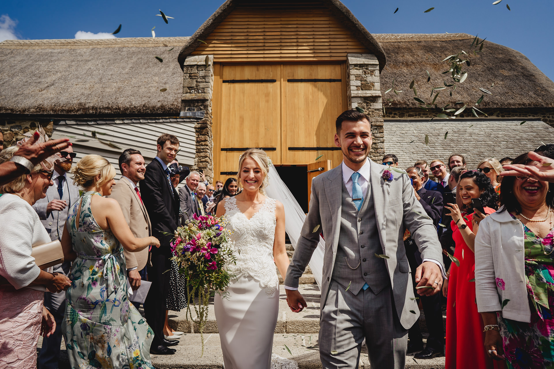 Bride and groom walking through confetti outside the great barn