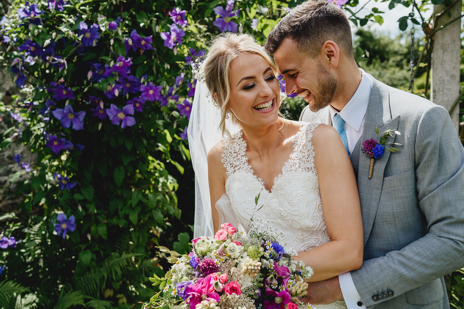 Bride and groom laughing together with purple flowers behind