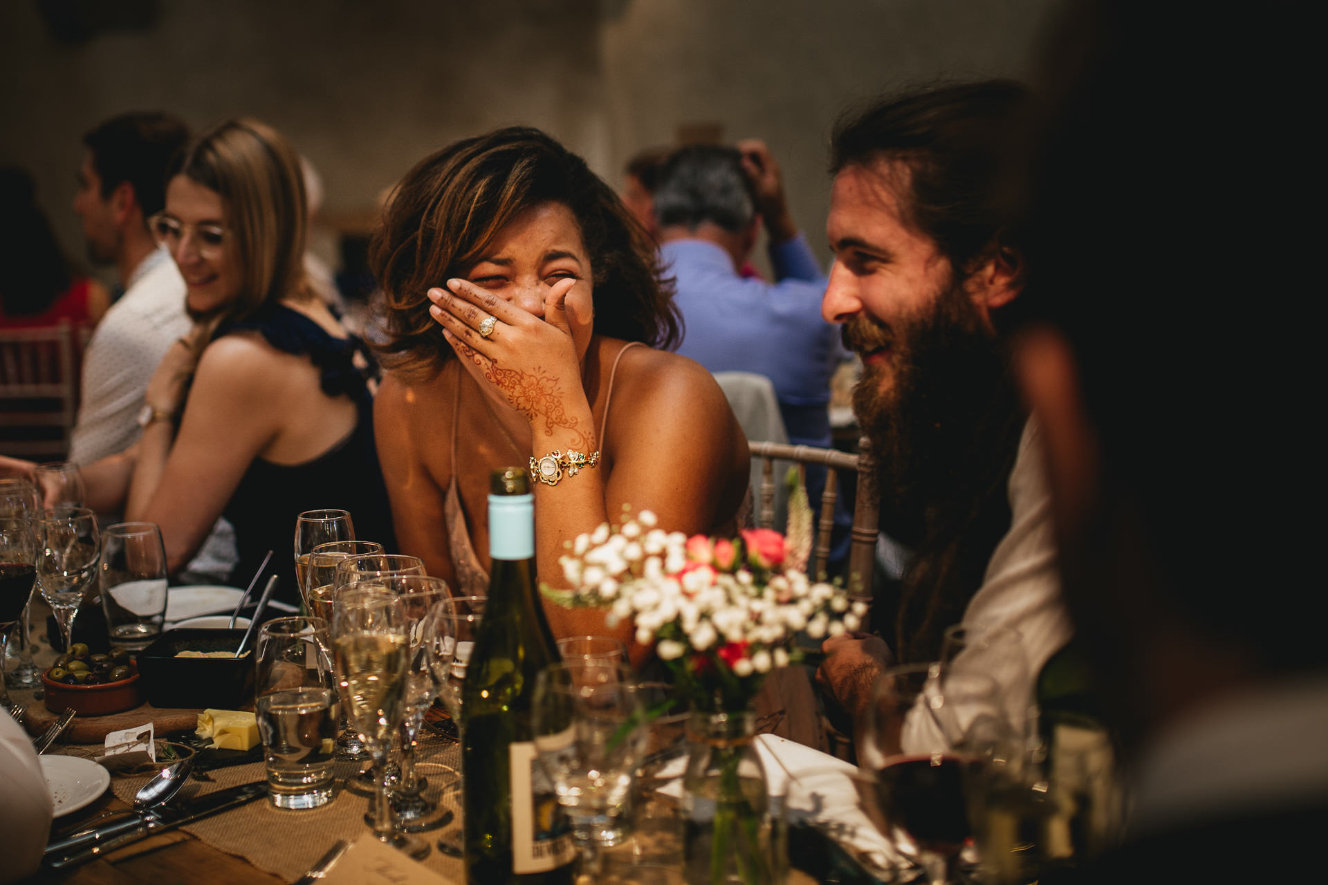 Guests laughing during wedding speeches in the great barn, devon