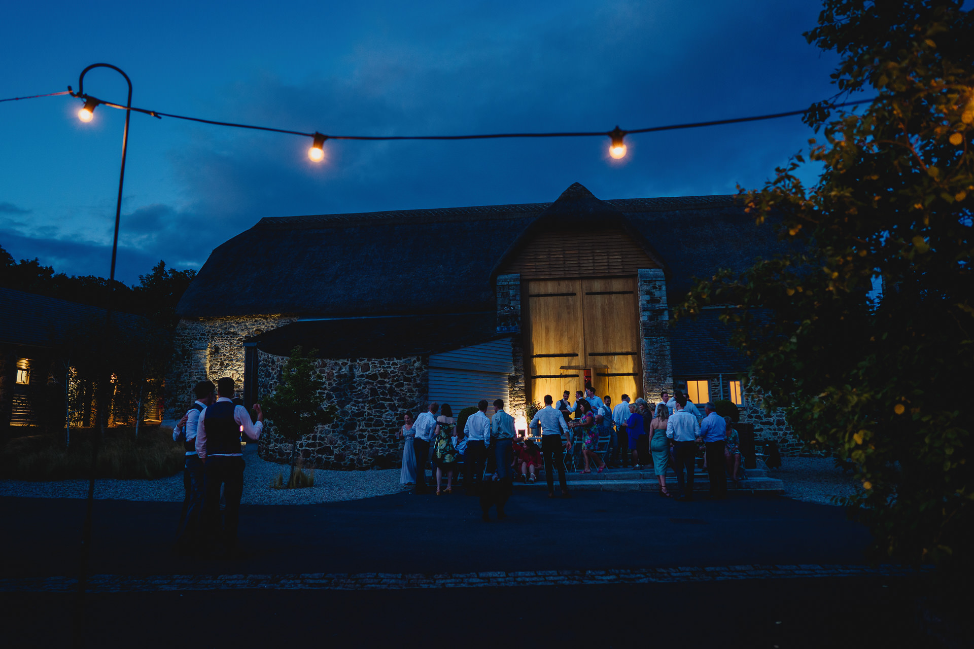 The Great Barn, Devon, in twilight, with wedding guests outside