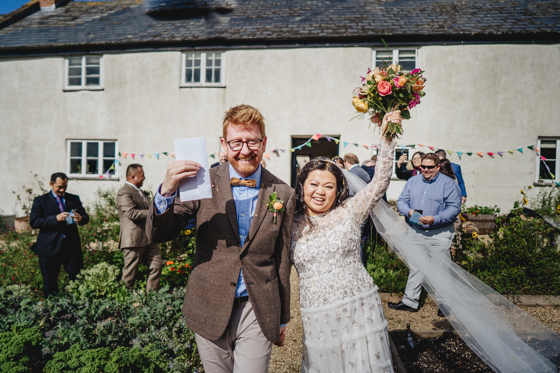 Bride and groom waving flowers and smiling after their outdoor wedding ceremony